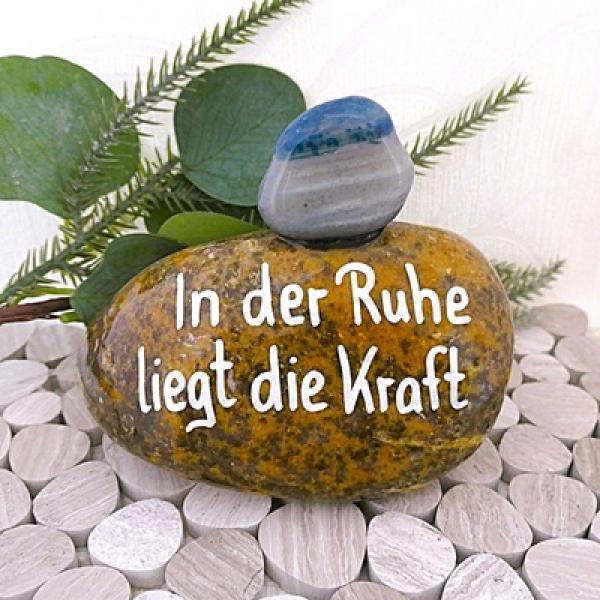 Glücksstein mit einem Spruch beschriftet und mit einem Trommelstein beklebt